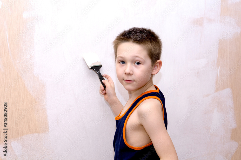 a boy in a blue t-shirt paints the interior wall of the apartment white and looks at the camera. the concept of home repair with your own hands. a boy in a blue t-shirt paints the interior wall of the apartment white and looks at the camera. the concept of home repair with your own hands.