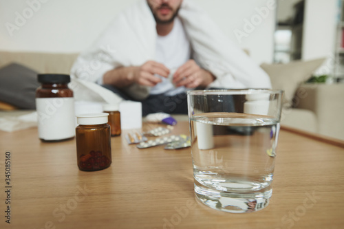 Glass of water, bottles with pills and blisters with tablets on wooden table