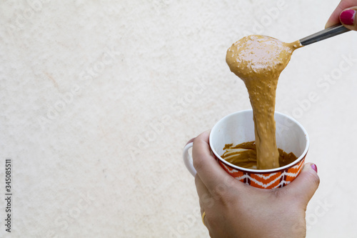 a girl showing hand beaten coffee paste in a colorful mug against plain wall background