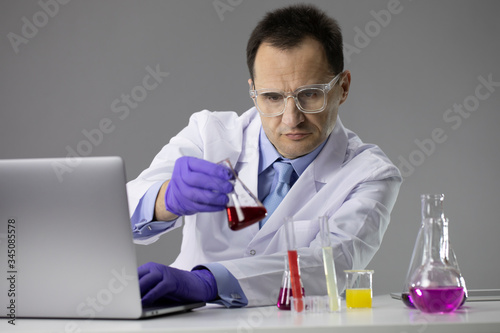 Scientist working at lab with test flasks and computer. Laboratory concept with attractive man biologist researcher synthesizing new compound. Biology laboratory workspace  science equipment concept
