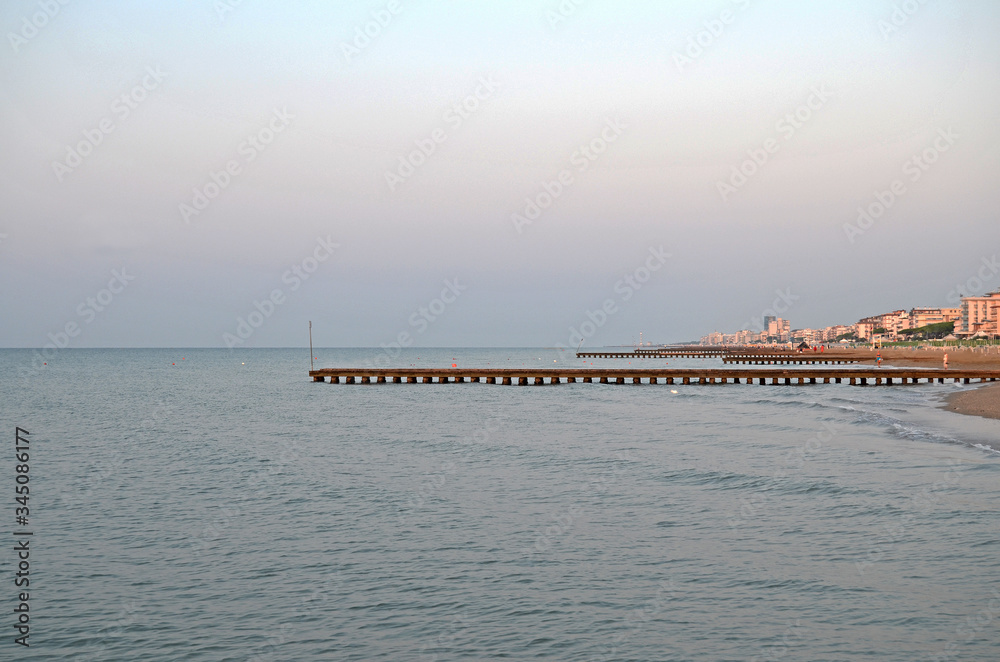 Fototapeta premium Beautiful coastline of the Adriatic Sea. Sunrise on the beach of Lido di Jesolo. Piers in the sea
