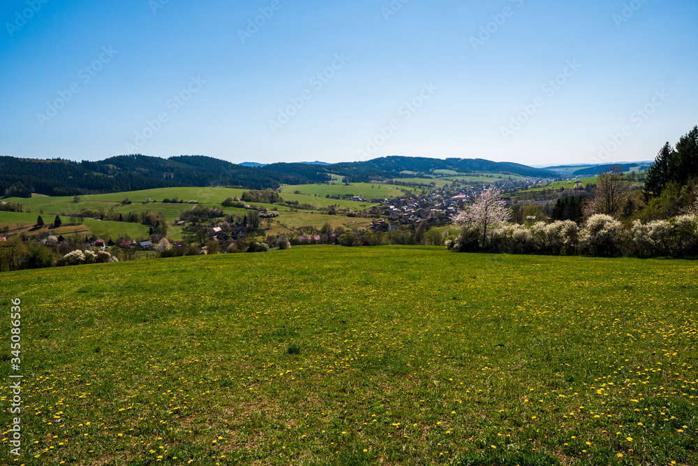 beautiful spring meadows in the mountains with a village in the valley, czech 