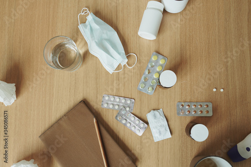 Wooden table with notebook, medical mask, tablets and pills, glass of water