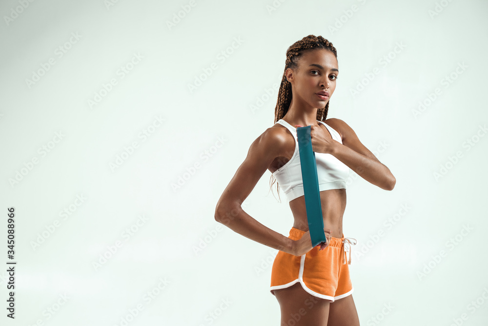 Fitness equipment. Pretty and young african woman in sport clothes showing  resistance band while standing in studio against grey background Stock  Photo | Adobe Stock