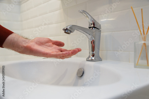 Man holding his hand under opened tap without water. Shutdown of water supply for non-payment or during repair work of the central system.