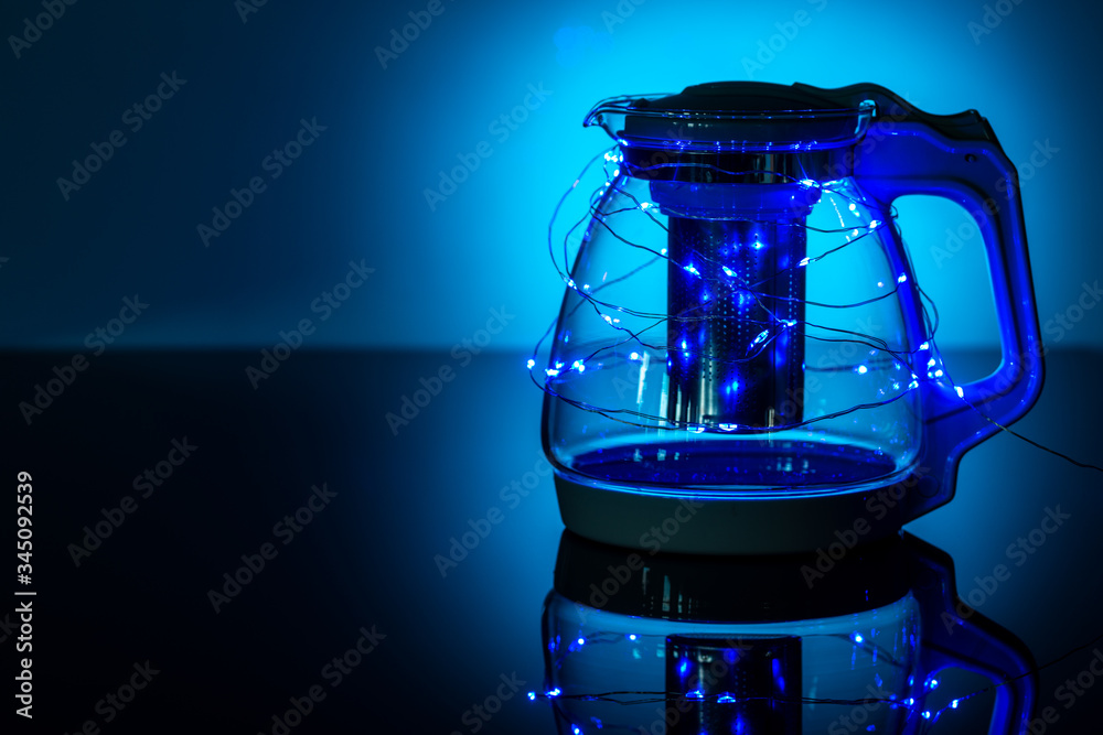 glass teapot on a dark blue background with a garland