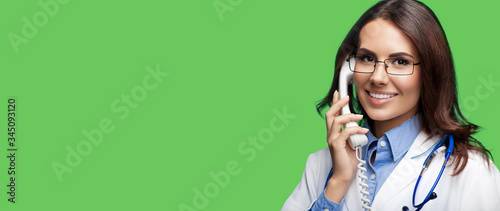 Portrait picture of happy smiling young doctor talking on phone, green color background. Copy space for some sign, slogan or advertising text. Medical call center service. photo