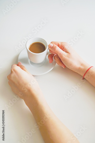 female hands holding a coffee mug and saucer over a white table