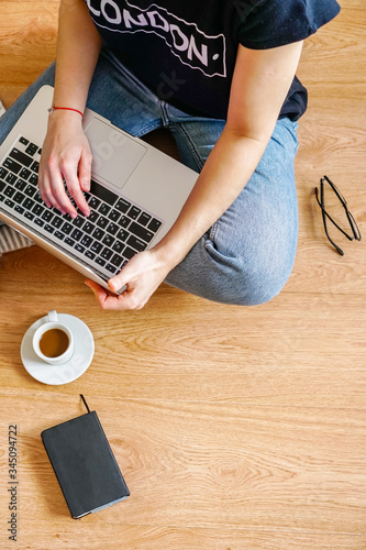 a girl sits on the floor with a laptop, near are glasses and a notebook for notes