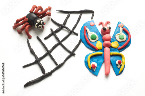 Spider caught a butterfly in its web. The scene is molded of multi-colored plasticine on white background