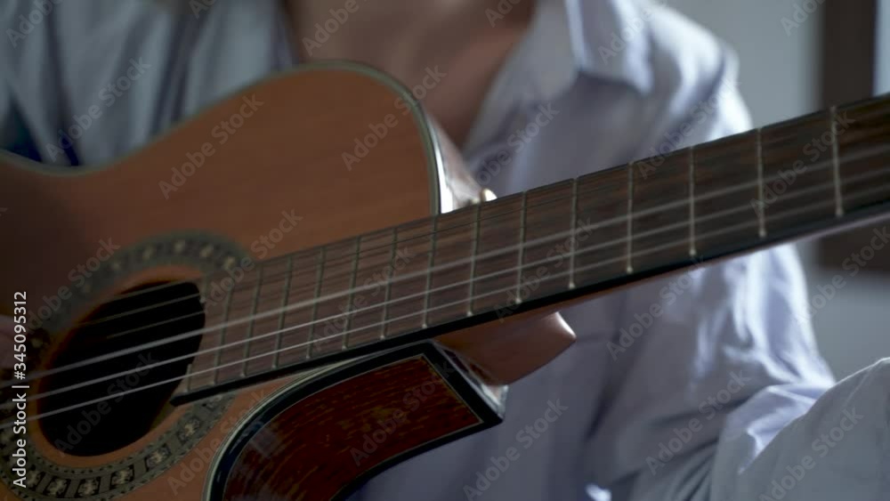 Panorámica hacia la derecha de las manos de una chica joven tocando la guitarra en su habitación. 