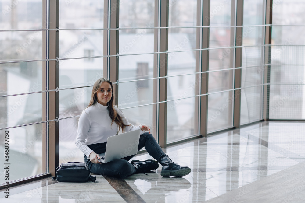 attractive girl working with laptop and things in airport terminal or office on floor. travel atmosphere or alternative work atmosphere. concept of alternative workplace and waiting.