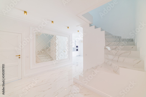 Hallway in a house with elegant open stairs in a modern interior. Modern LED lamps. Large space and beauty. Stairs of Italian stone tiles
