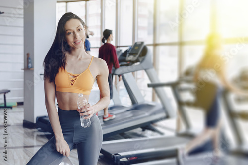 young attractive girl in the gym drinking water on the background of treadmills