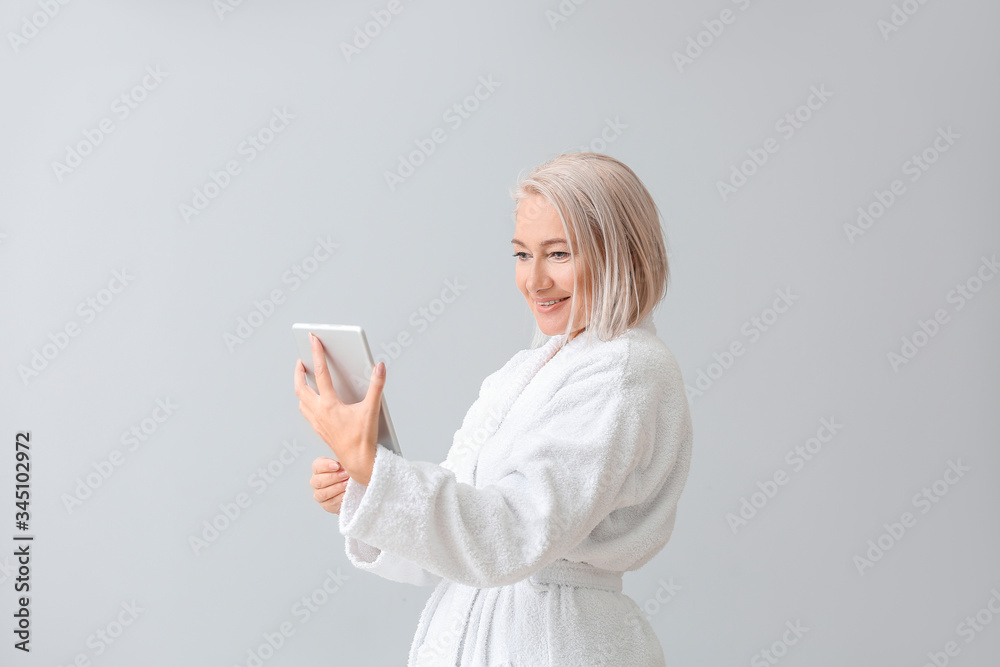 Happy mature woman in bathrobe and with tablet computer on grey background Happy mature woman in bathrobe and with tablet computer on grey background
