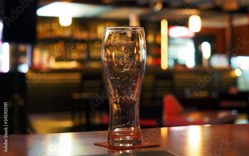 Evening. Empty beer glass on the table in a dark bar, panoramic view. Foam stains inside the glass