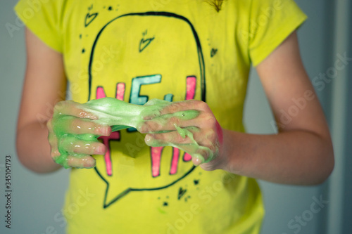 Young girl getting her hands stuck with a sticky green slime.