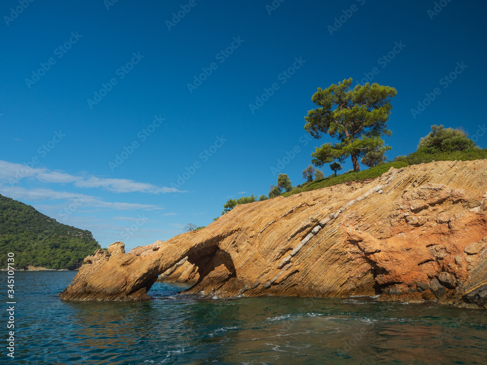View of the coast from the sea. Amazing color of water, beautiful rocks with trees growing on them. Rock arch. Bright sunny summer day.