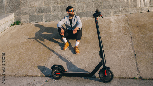 Young hipster man in a suit riding an electric scooter in bright sunny day. Ecological transportation concept.