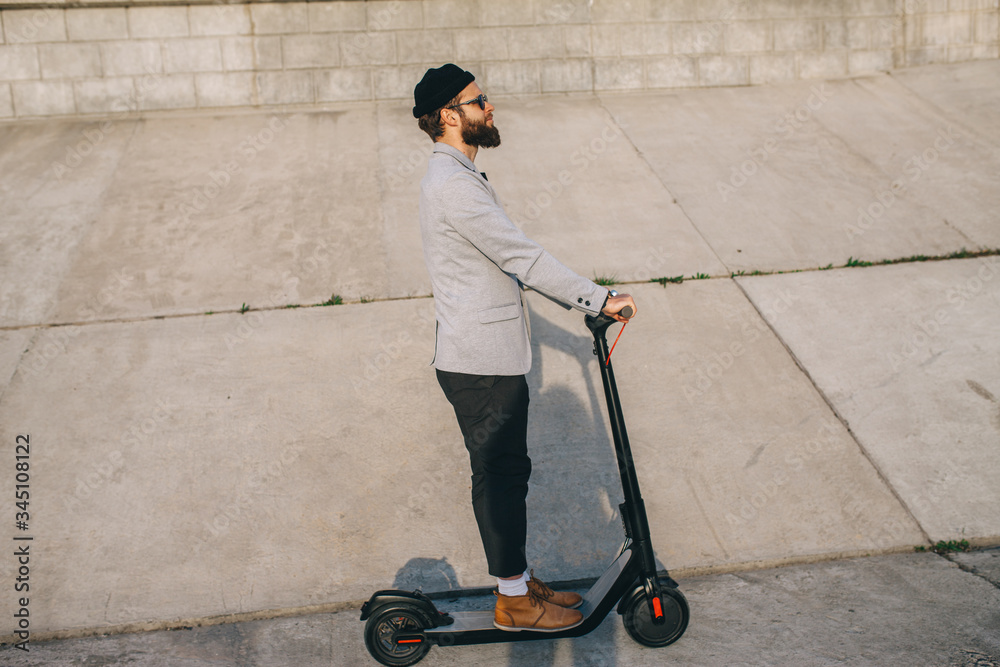 Young hipster man in a suit riding an electric scooter in bright sunny day. Ecological transportation concept. Young hipster man in a suit riding an electric scooter in bright sunny day. Ecological transportation concept.