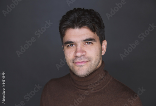a young dark man in a turtleneck is smiling against a dark background