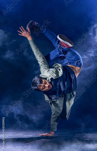 A street dancer stands on one hand against a dark background in a cloud of smoke