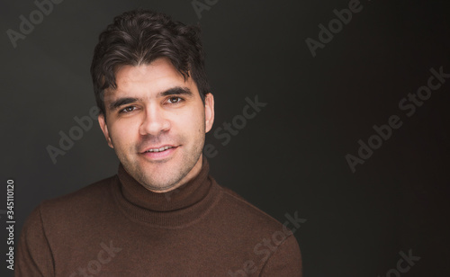 a young dark man in a turtleneck is smiling against a dark background