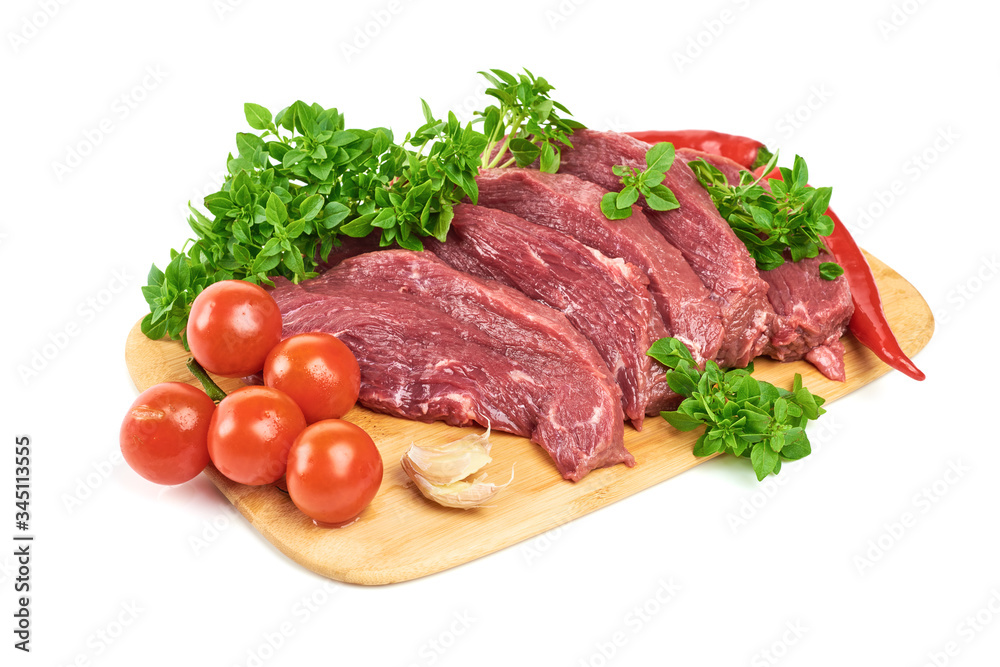 Slicing fresh meat steaks, with young basil, red pepper, garlic and cherry tomatoes on a cutting board on a white background. Fresh flank steak. The view from the top.