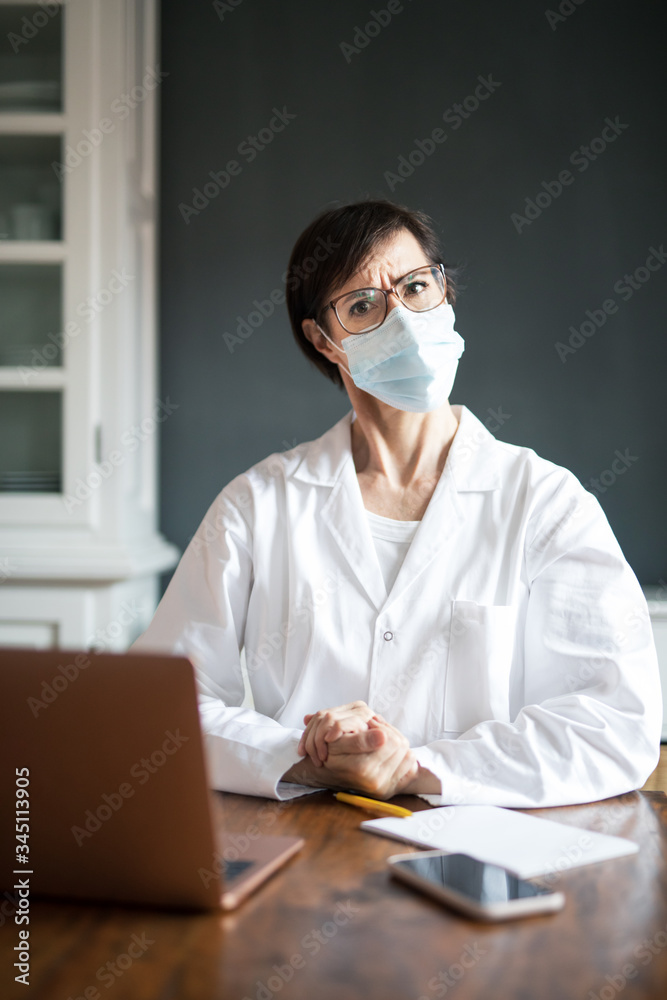 Frau arbeitet in Arztkittel und Mundschutz im Homeoffice oder Praxis zuhause. Frau arbeitet in Arztkittel und Mundschutz im Homeoffice oder Praxis zuhause.