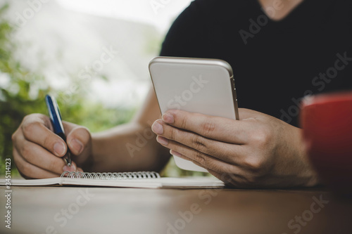 man relaxed writing and working with digital mobile smart phone, report document with red coffee cup on desk at cafe restaurant, work from home, digital technology, internet, online business concept