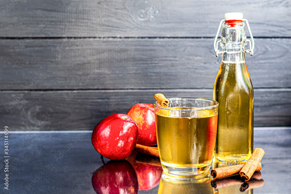 Healthy organic foods. Apple cider in a glass bowl and fresh red apples on a black background. In a glass of ice cubes and nearby cinnamon sticks. Healthy organic foods. Apple cider in a glass bowl and fresh red apples on a black background. In a glass of ice cubes and nearby cinnamon sticks.