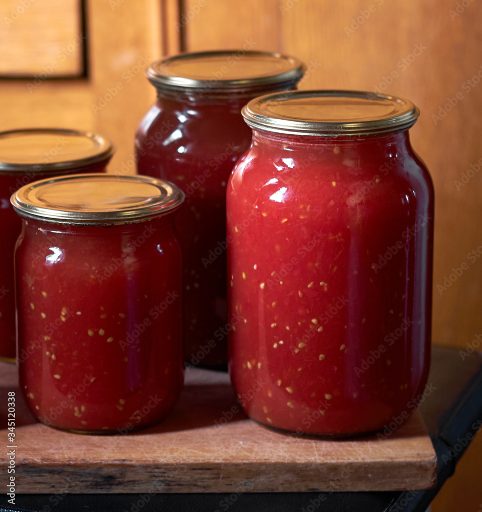 Preserving of tomato paste or juice, homemade vitamin drink in glass jars on wooden board, closeup, copy space, vertical, homegrown healthy food concept Preserving of tomato paste or juice, homemade vitamin drink in glass jars on wooden board, closeup, copy space, vertical, homegrown healthy food concept
