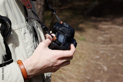 man holds a camera in his hands in the forest in the sunlight 