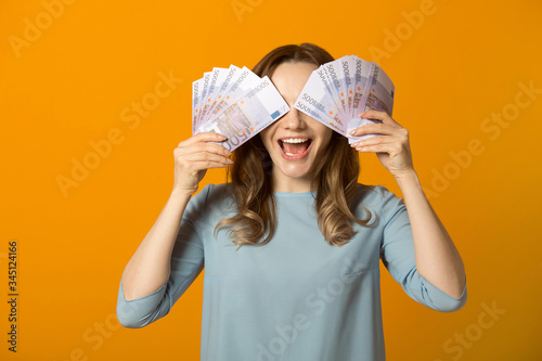 beautiful young woman in a dress on a yellow background with euro in hands