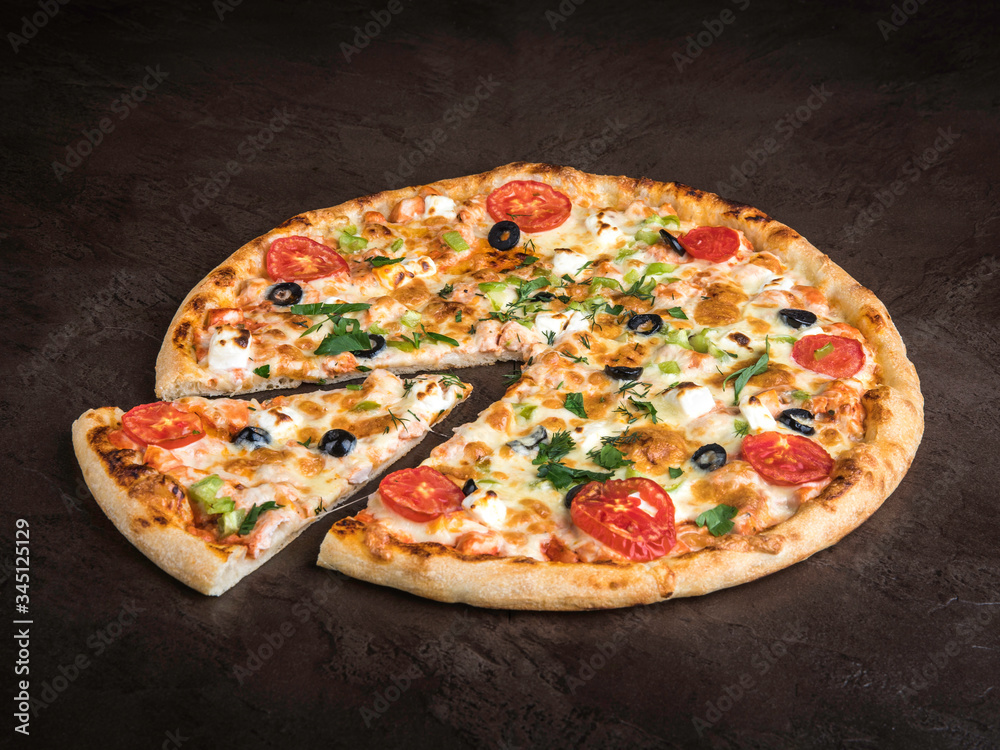 Delicious pizza with chicken, cheese, tomatoes and olives lies on a dark stone surface
