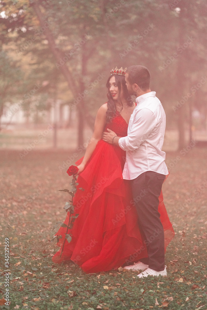 Beautiful romantic couple. Attractive young woman in red dress and crown with handsome man in white shirt are in love on pink smoke. Saint Valentine's Day. Pregnant and wedding concept.