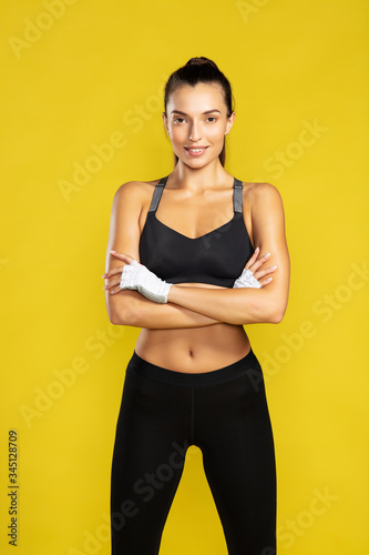 Ready for workout. Young beautiful woman in sportswear keeping arms crossed and looking at camera while standing against yellow background © Kostiantyn