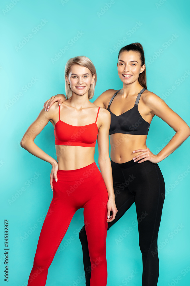 Always in good shape. Two young and beautiful sporty girls in sportswear looking at camera while standing against blue background