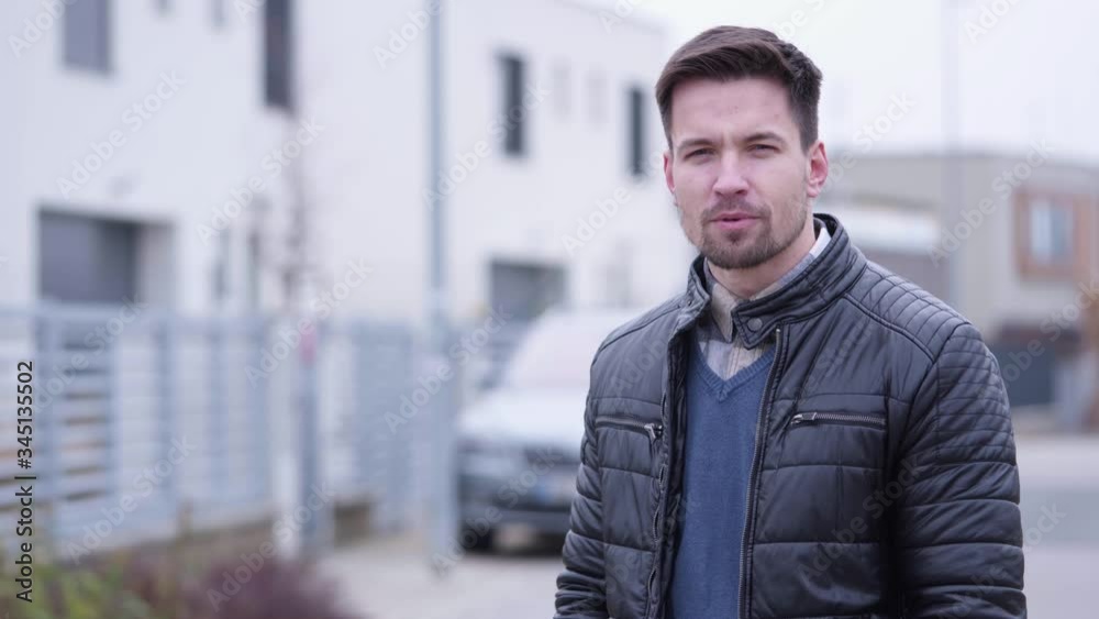 A young handsome man talks to the camera in a street with a house in the blurry background - closeup A young handsome man talks to the camera in a street with a house in the blurry background - closeup