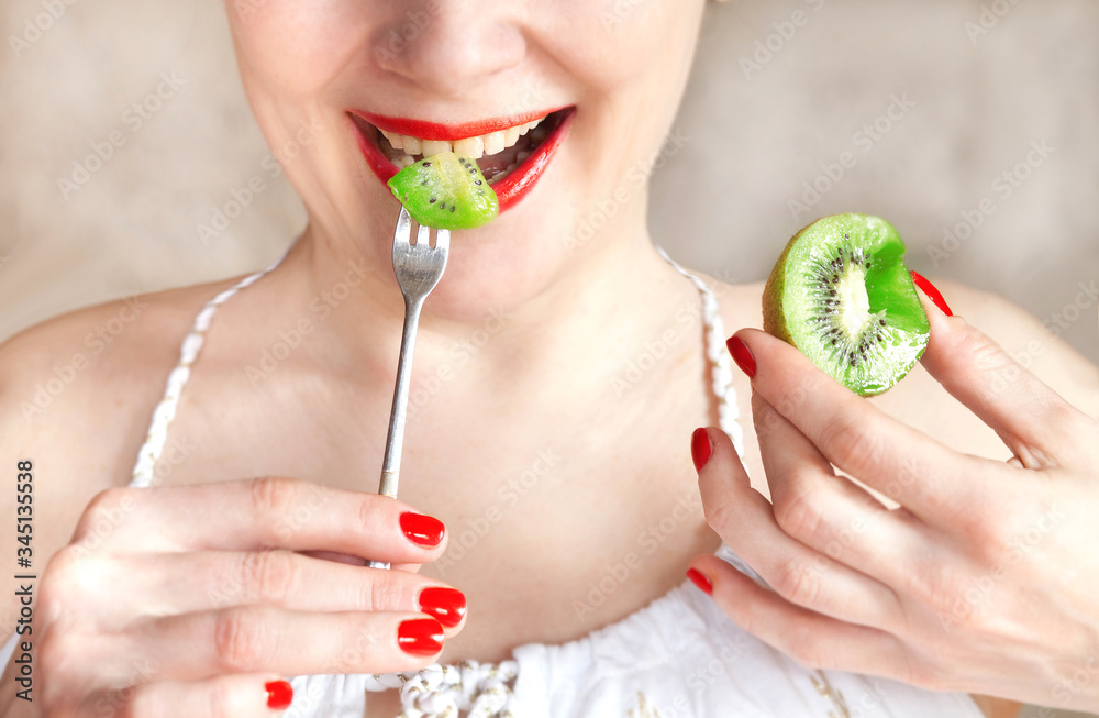girl with red lipstick eats a ripe kiwi close up