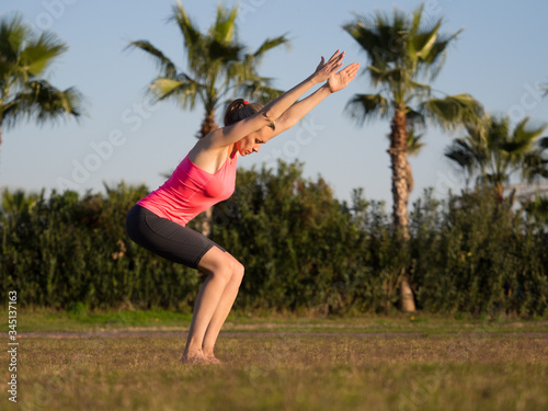 Evening yoga. Fit caucasian woman practice chair pose on the grass outdoor in summer, selective focus.