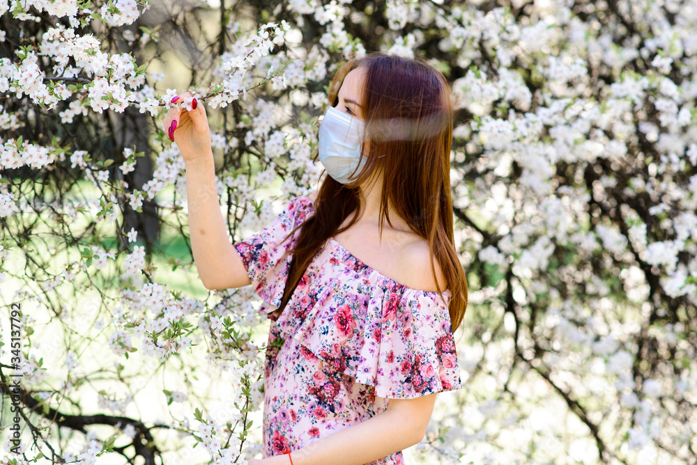 Girl, young woman in a protective sterile medical mask on her face in the spring garden. Air pollution, virus, pandemic coronavirus concept. Girl, young woman in a protective sterile medical mask on her face in the spring garden. Air pollution, virus, pandemic coronavirus concept.