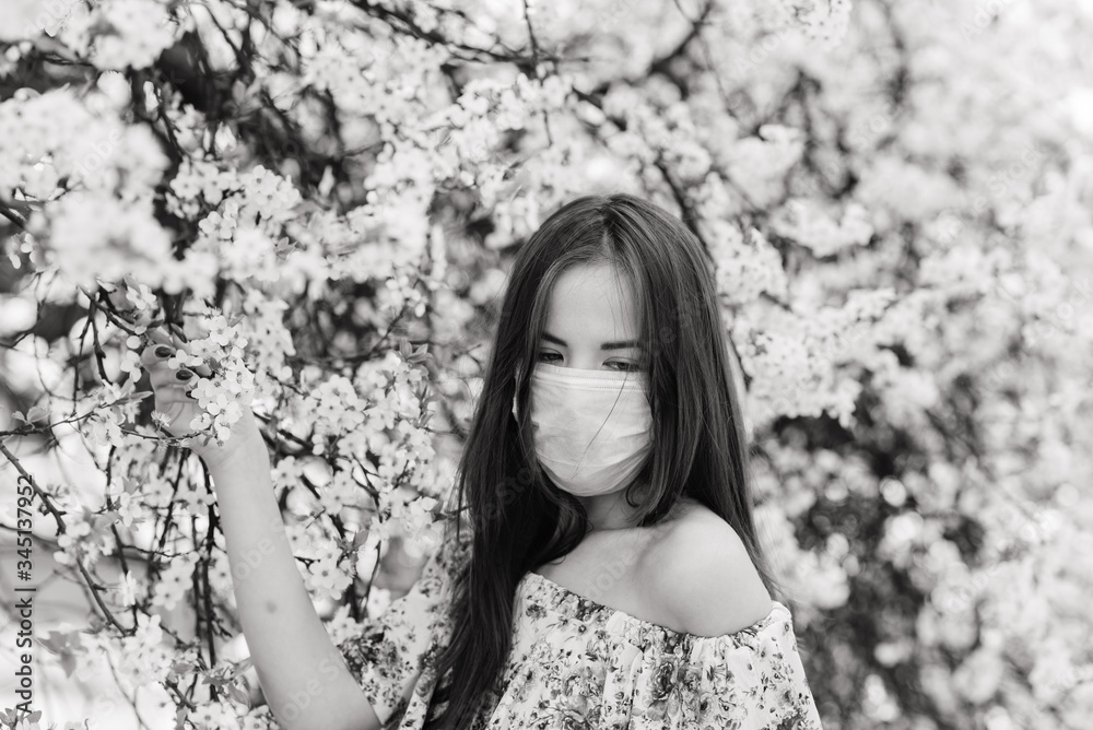 Girl, young woman in a protective sterile medical mask on her face in the spring garden. Air pollution, virus, pandemic coronavirus concept. Girl, young woman in a protective sterile medical mask on her face in the spring garden. Air pollution, virus, pandemic coronavirus concept.