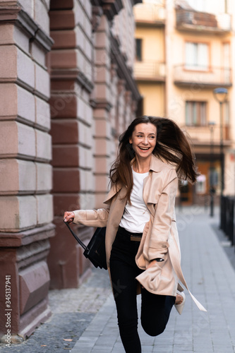 Outdoor photo of brunette lady walking on street background in autumn day.Fashion street style portrait. wearing dark casual trousers, white sweater and creamy coat.Fashion concept.