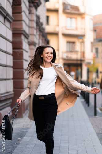 Obraz na płótnie Outdoor photo of brunette lady walking on street background in autumn day.Fashion street style portrait. wearing dark casual trousers, white sweater and creamy coat.Fashion concept. w salonie