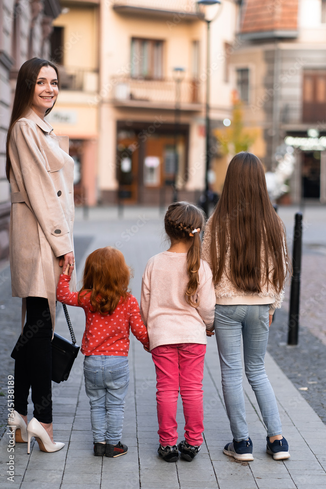 Obraz premium Happy family. mother of many children and three daughters child girl together, walking and joyfully laughing while relaxing on park on a summer holiday. Family outdoors lifestyle. Back view