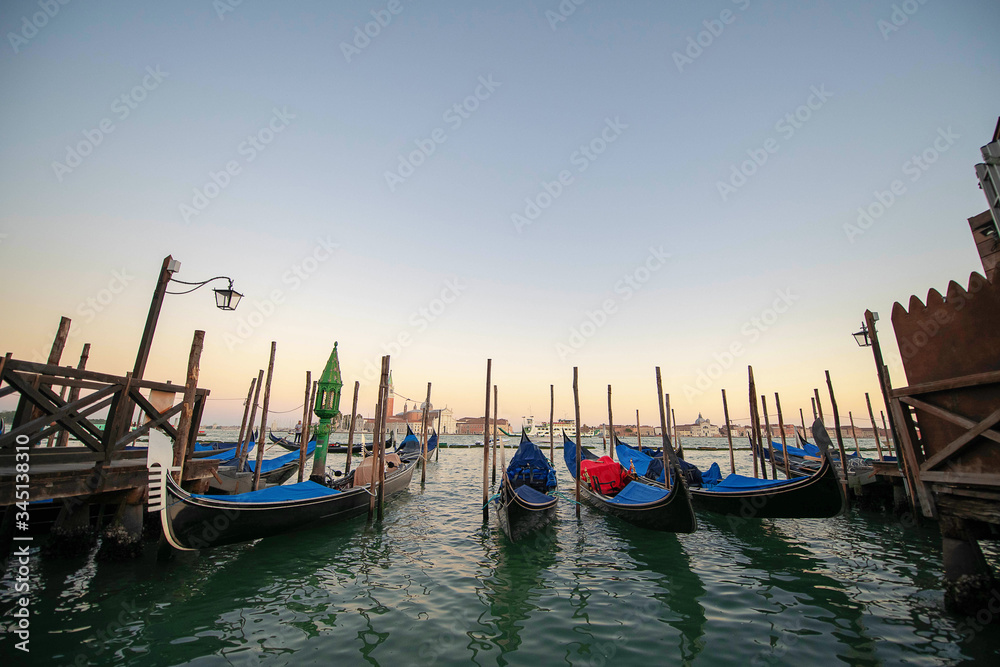 Several gondolas moored nearby Saint Mark square, early morning, tranquil sunrise atmosphere, usually serving tourists for transportation around the narrow canals, in Venice, Italy