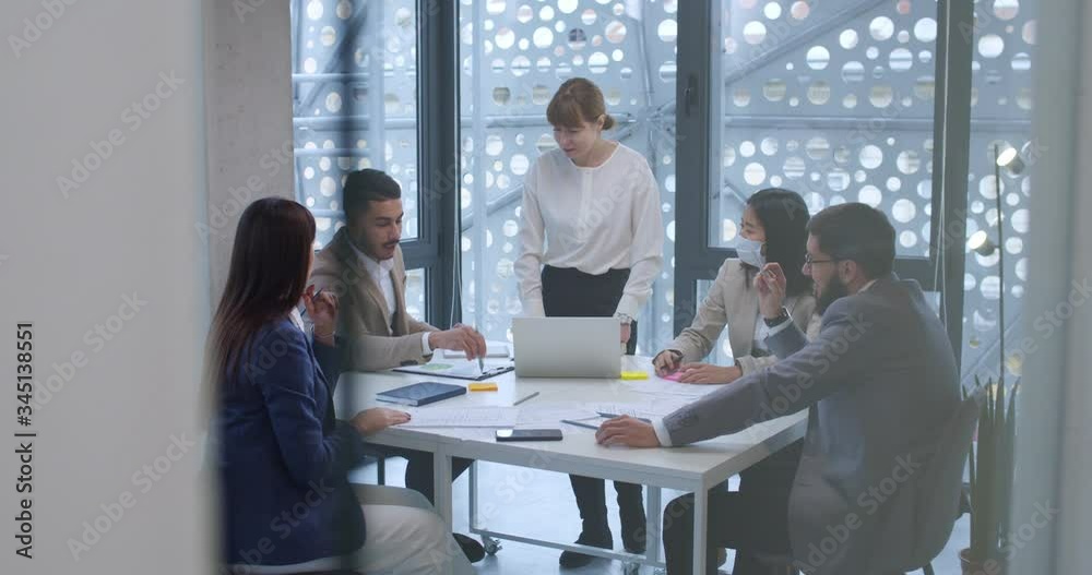View over glass wall on business meeting of multiethnic firm co-workers sitting at desk in office. Businessmen and businesswomen talking and making decisions under supervision of female boss. View over glass wall on business meeting of multiethnic firm co-workers sitting at desk in office. Businessmen and businesswomen talking and making decisions under supervision of female boss.