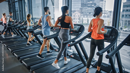 Group of Five Athletic People Running on Treadmills, Doing Fitness Exercise. Athletic and Muscular Women and Men Actively Workout in the Modern Gym. Sports People Workout in Fitness Club. Side View
