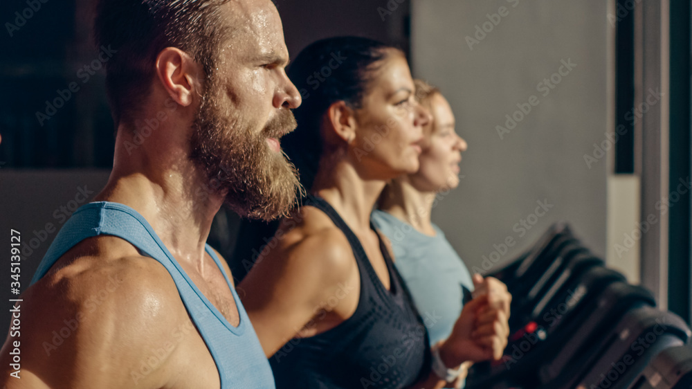 Shot of Athletic Man Running on Treadmill, Doing Fitness Exercise. Athletic and Muscular Women and Men Actively Training in the Modern Gym. Side View Golden Hour Sunny Light Shot of Athletic Man Running on Treadmill, Doing Fitness Exercise. Athletic and Muscular Women and Men Actively Training in the Modern Gym. Side View Golden Hour Sunny Light